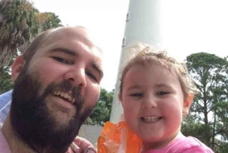 Father and child smiling in front of a lighthouse