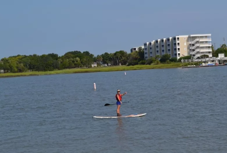 Person waving from a paddle board in calm, flat water